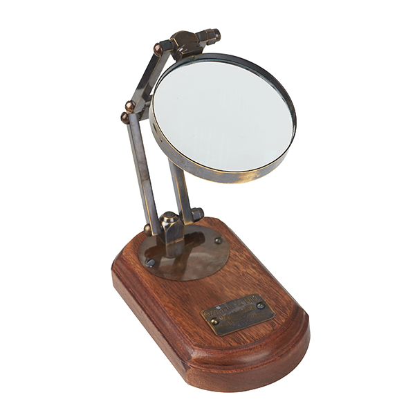 זכוכית מגדלת על זרוע נחושת מתקפלת על בסיס עץ. 
קוטר זכוכית 7.5 ס